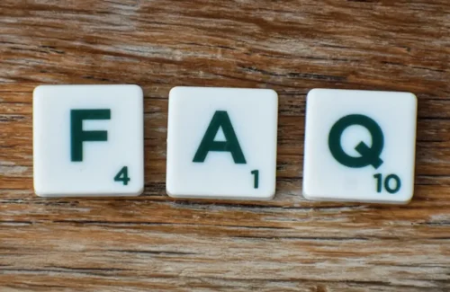 Die Buchstaben F A und Q auf Scrabble-Buchstaben, die auf einem Untergrund aus Holz liegen.